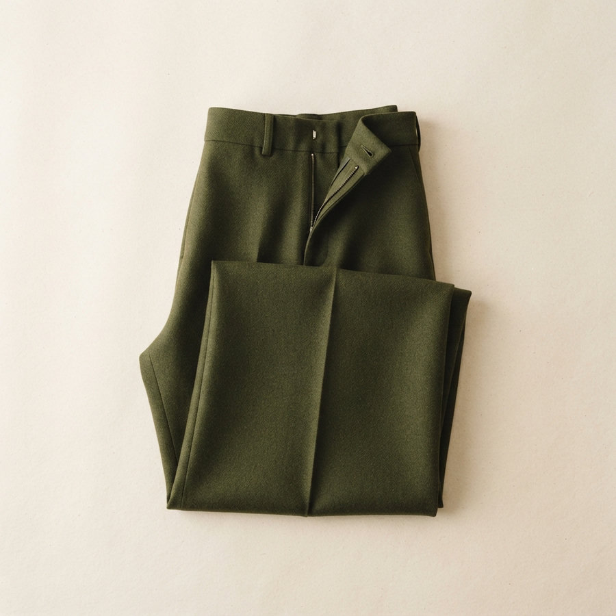 A pair of folded deep-olive wide-leg wool trousers on a warm paper background.
